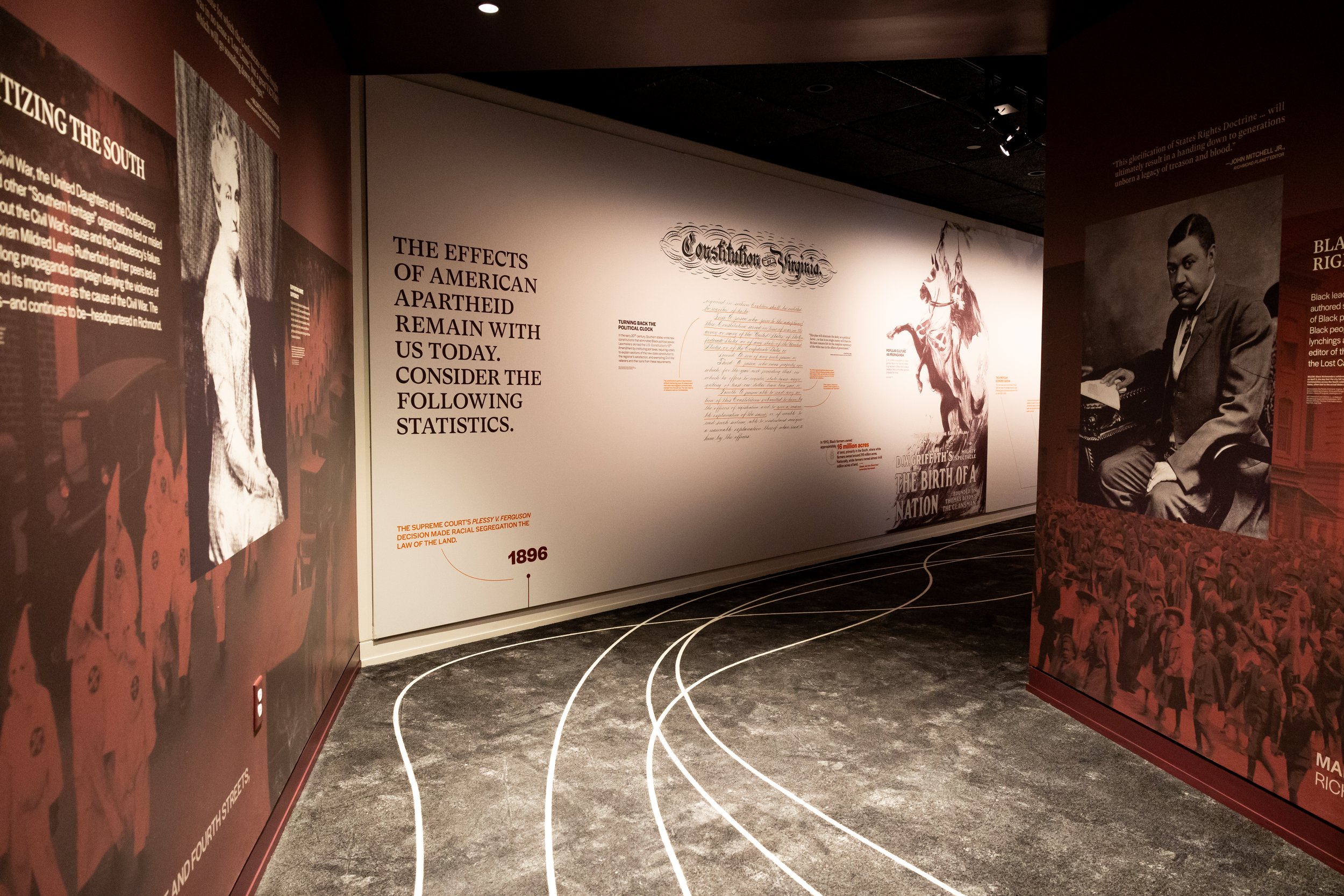 Exhibit wall with text about the history and effects of American apartheid, including photographs of historical figures and scenes, and a timeline on the floor.