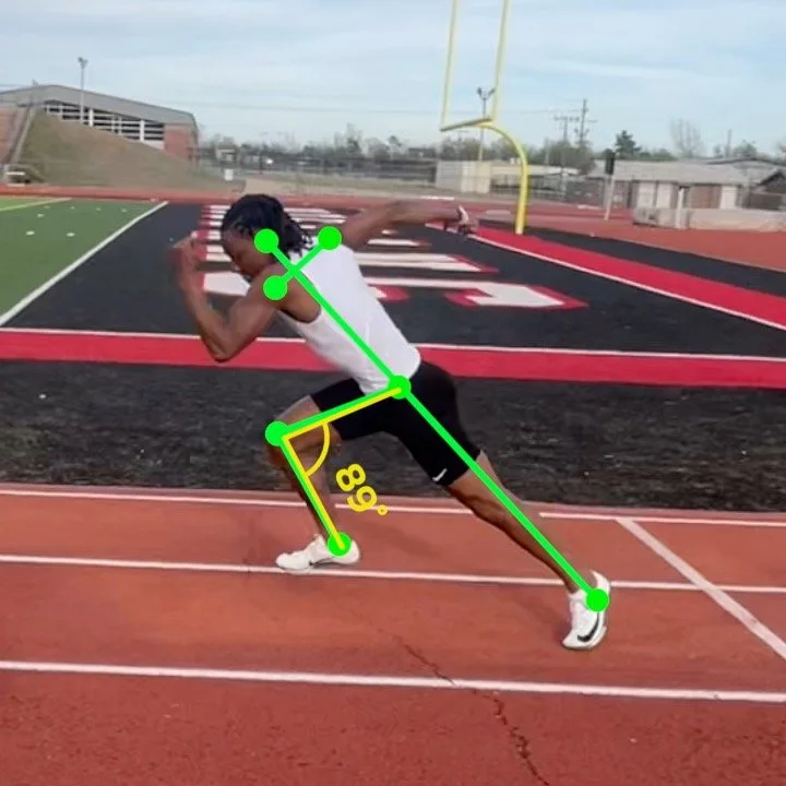 Athlete in a start position on a track with a field and goalpost in the background.