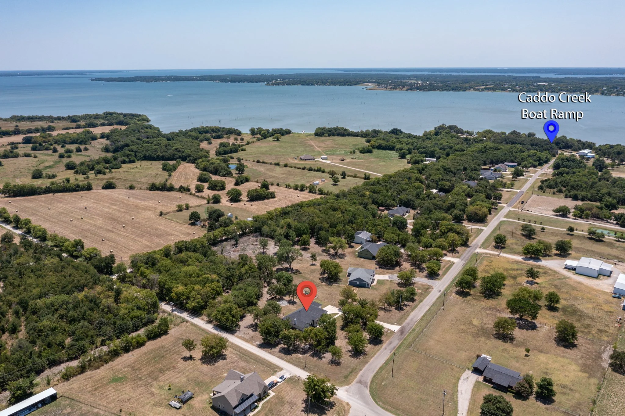 Aerial view of rural landscape with houses, trees, farmland, and Caddo Creek Boat Ramp by a large body of water.