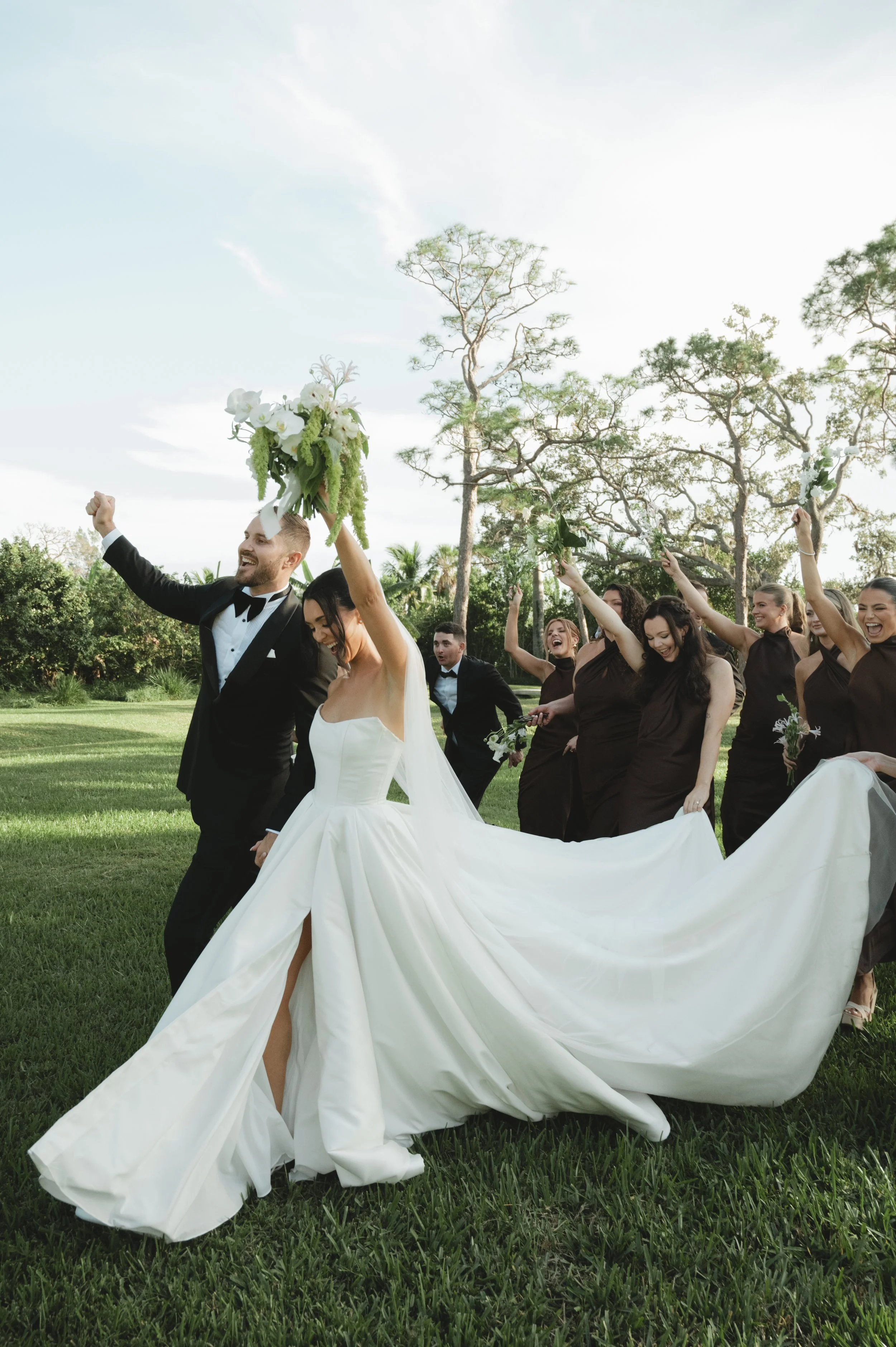 A newlywed couple cheering and celebrating with their bridal party that walks behind them.