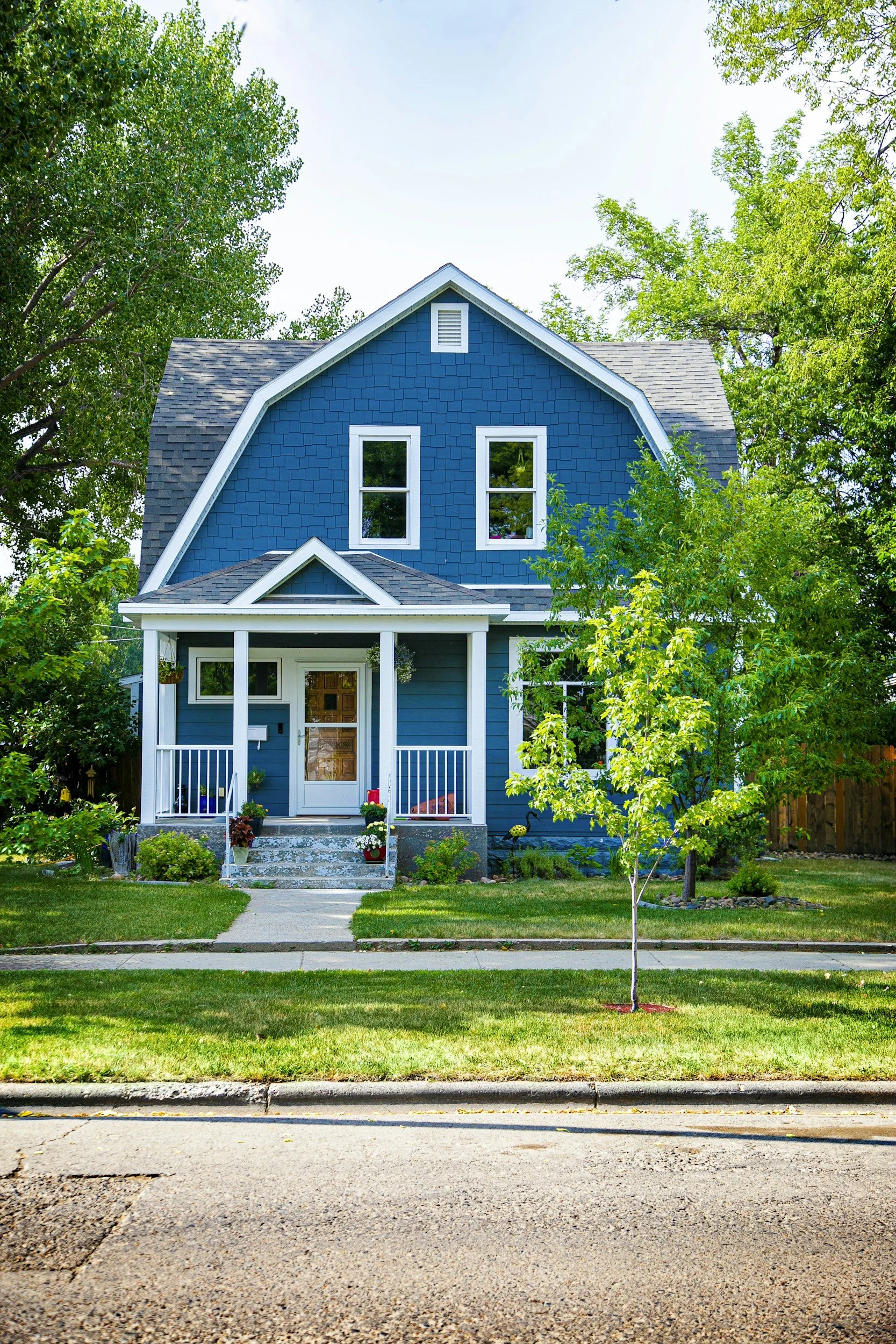 A two-story blue house with white trim, a small porch, and a front yard with grass, trees, and potted plants in Crescent Hill area of Louisville. Crescent Hill Real estate. Clifton real estate.