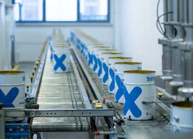 Rows of paint cans with blue and yellow labels on a conveyor belt in a factory setting.