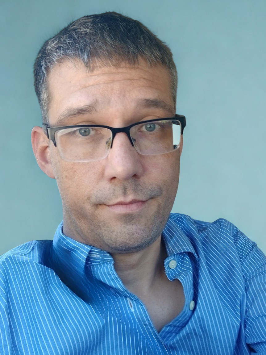 Close-up of Nicholas Bennett, LGSW, who has short brown hair, glasses, and a blue striped button-up shirt.