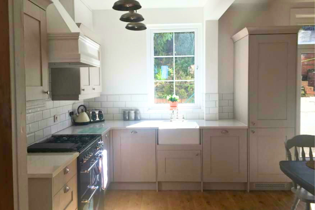 Kitchen with white cabinets, a black stove, a white farmhouse sink beneath a window with greenery outside, and a black and white ceiling light fixture.