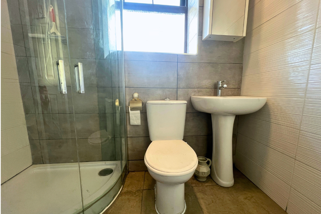 Small bathroom with a shower on the left, toilet in the middle, and a sink on the right. There is a window above the toilet and a cabinet above the sink.