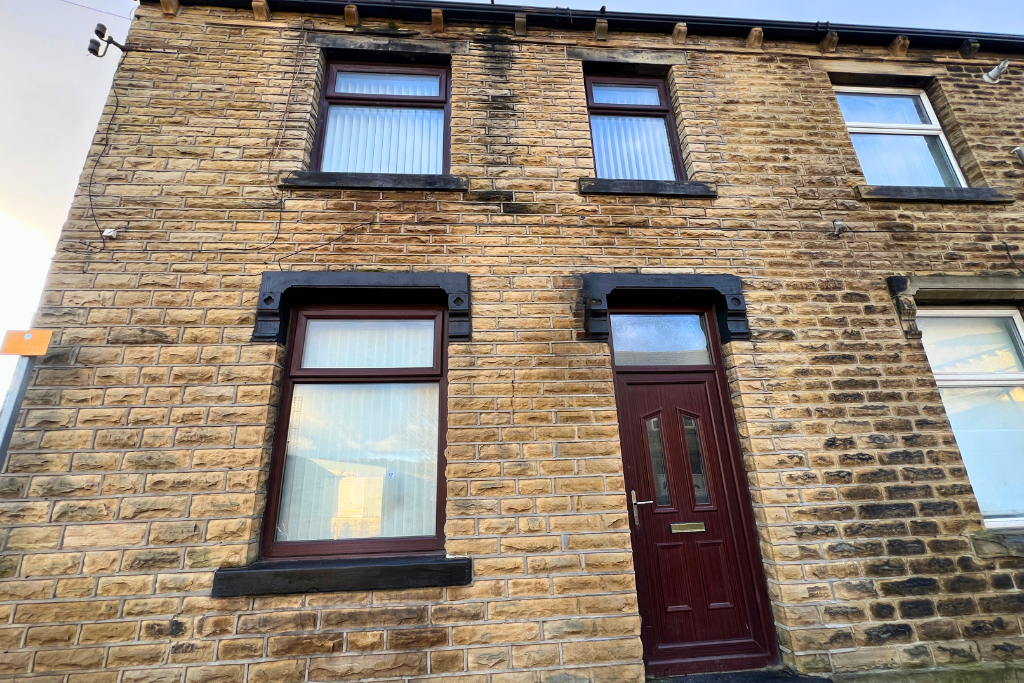 A two-story brick house with three windows on the front and a maroon door, with black accents around the windows and door.