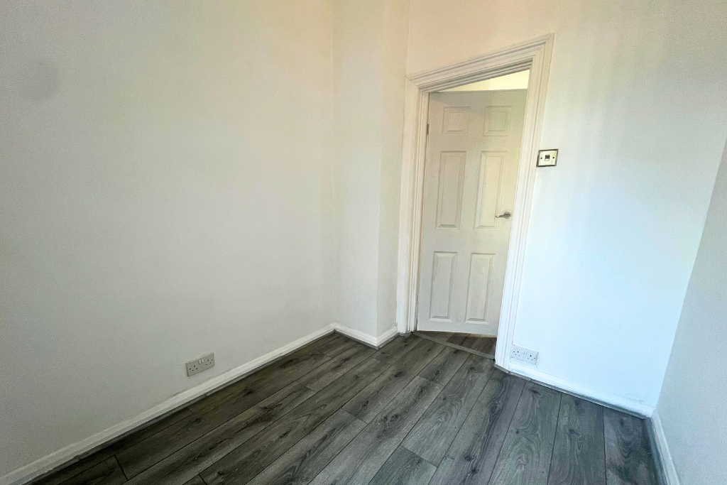 Empty room with white walls, a closed white door, wood flooring, and electrical outlets.