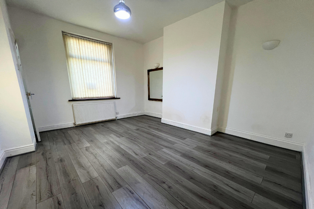 Empty room with white walls, a window with blinds, a radiator, a mirror, and a ceiling light.
