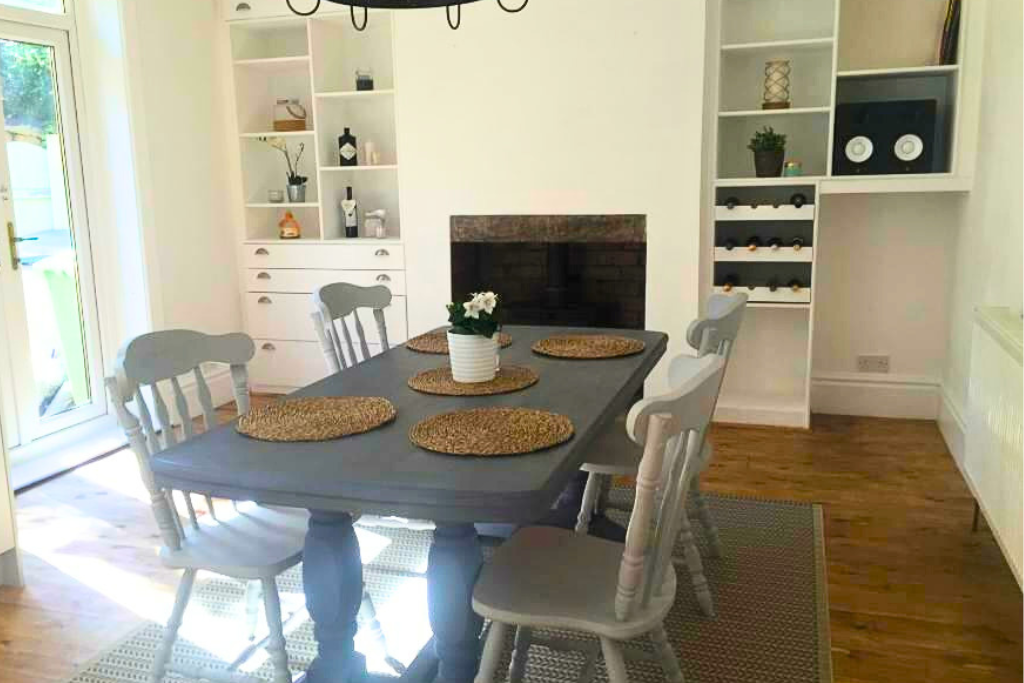 Dining room with a table and six chairs, a small potted plant on the table, a brick fireplace, and built-in shelves with decorative items and wine bottles.