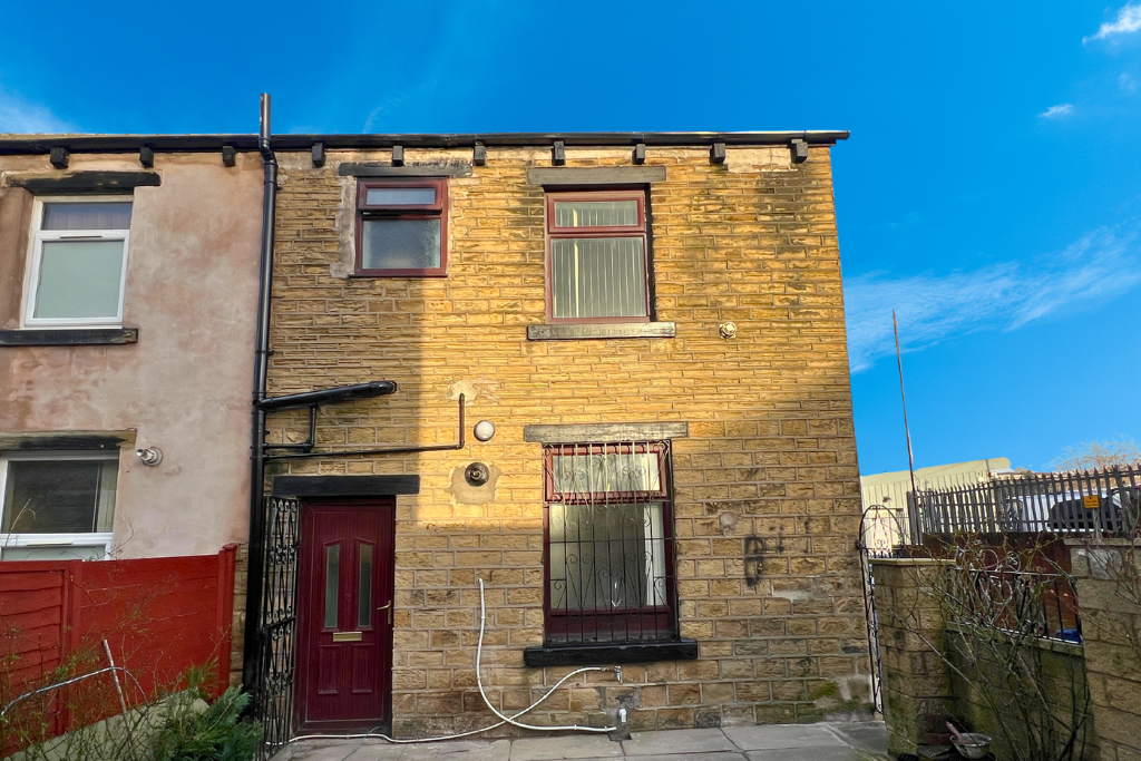 A brick two-story house with burgundy window frames and door, black accents, a metal gate, and a bright blue sky.