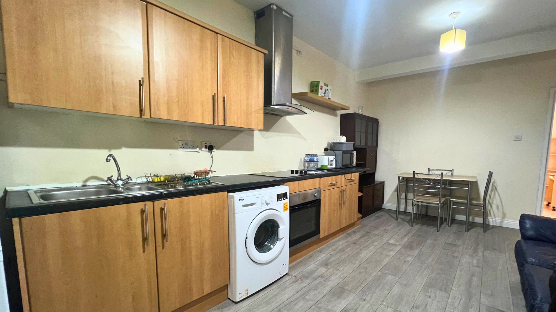 Interior of a kitchen with wooden cabinets, a sink, countertop appliances, and a dining area with a table and chairs.