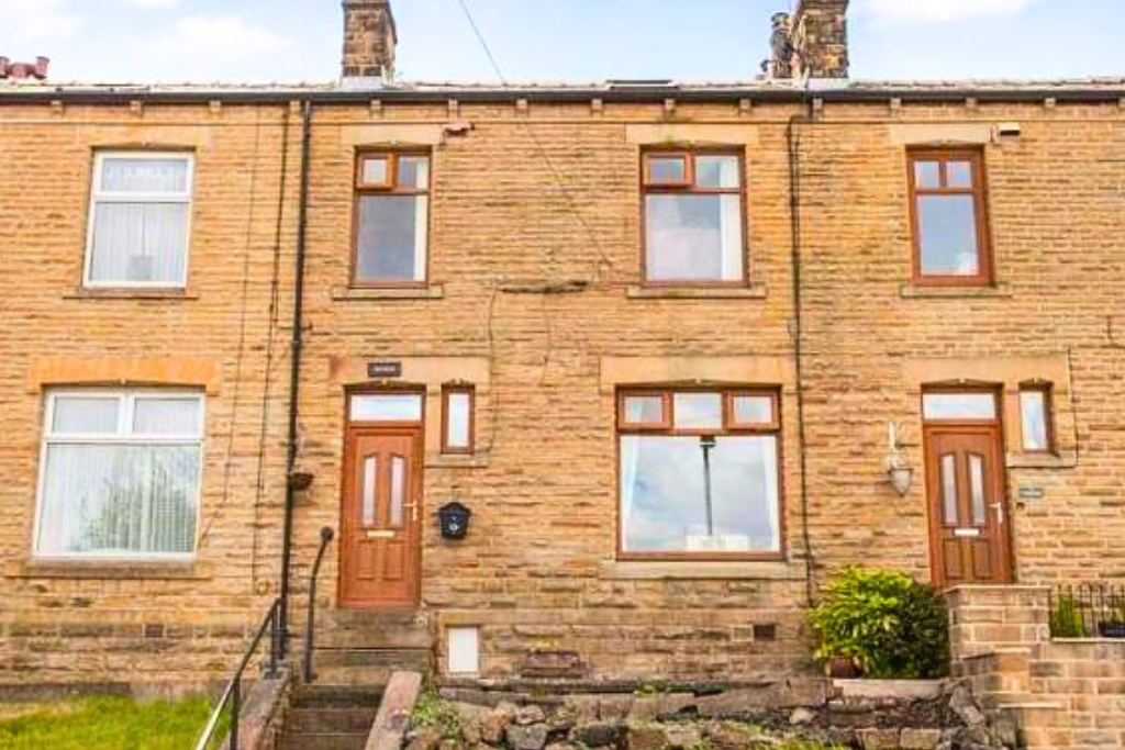 Front view of a brick terraced house with three floors, two doors, multiple windows, a small front yard with steps, and a lamp fixture.