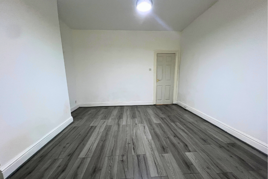 Empty room with white walls, dark wood flooring, a small window, and a closed door.