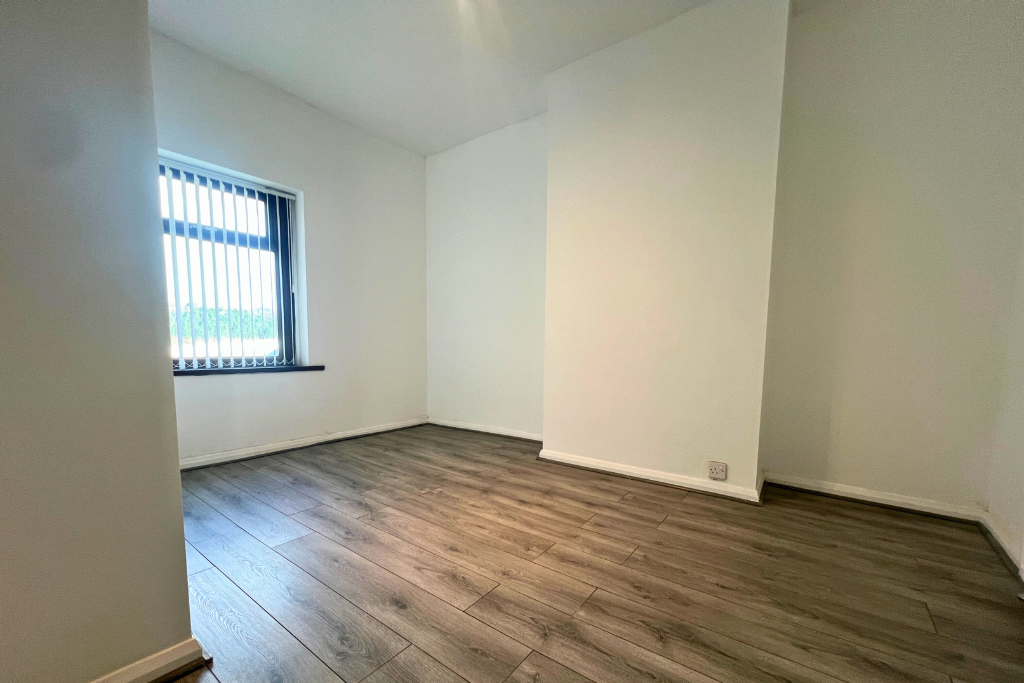 Empty room with wooden flooring, a window with vertical blinds, and white walls.