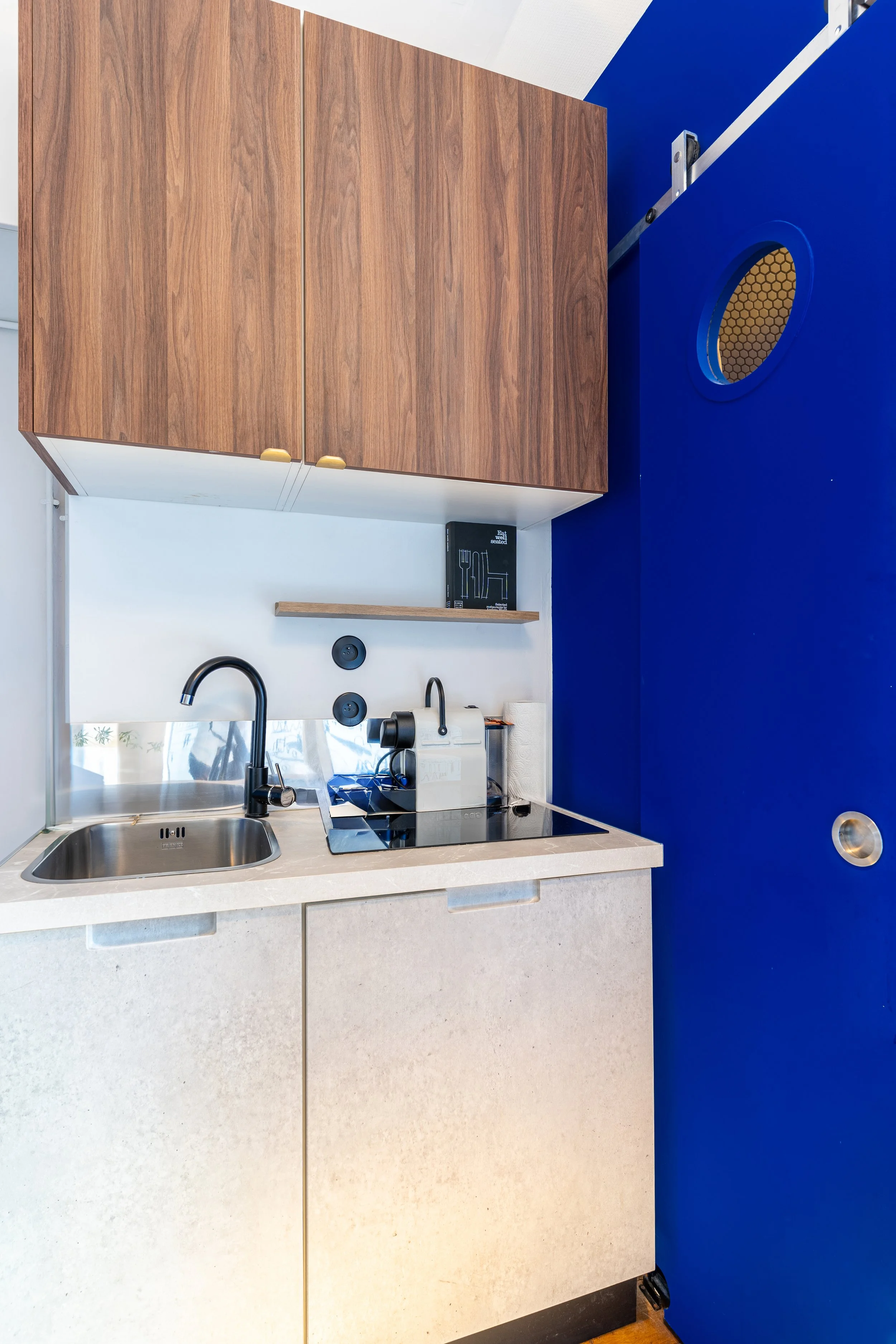 Kitchen with beige countertop, black sink, black faucet, white cabinetry, black stovetop, gray backsplash, wooden cabinets, and a bright blue wall.