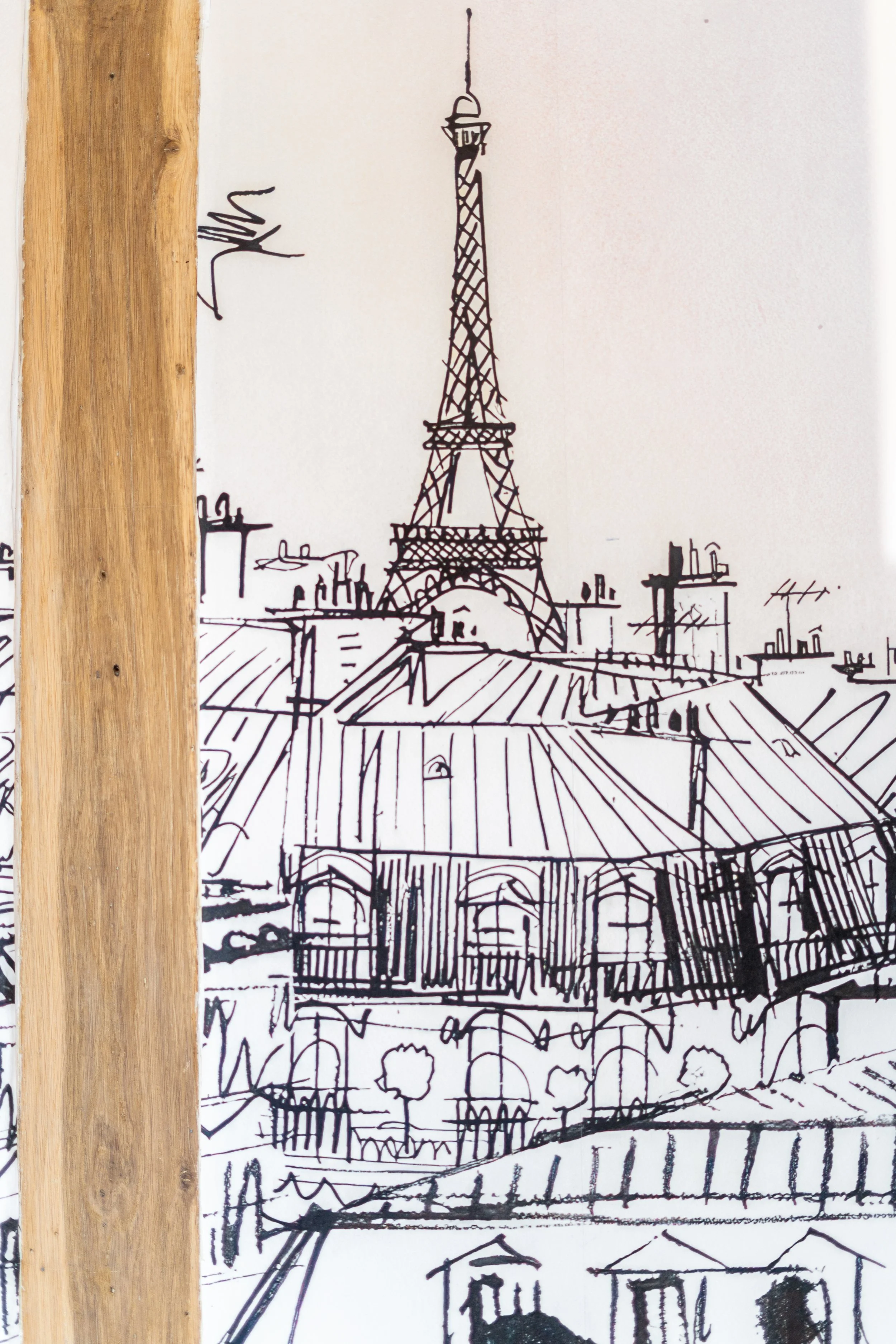 A black ink sketch of the Eiffel Tower and Paris rooftops on white paper, partially obscured by a wooden vertical strip on the left side.