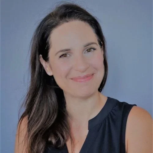 A woman with long dark hair smiling at the camera, wearing a sleeveless navy blue top against a light blue background.