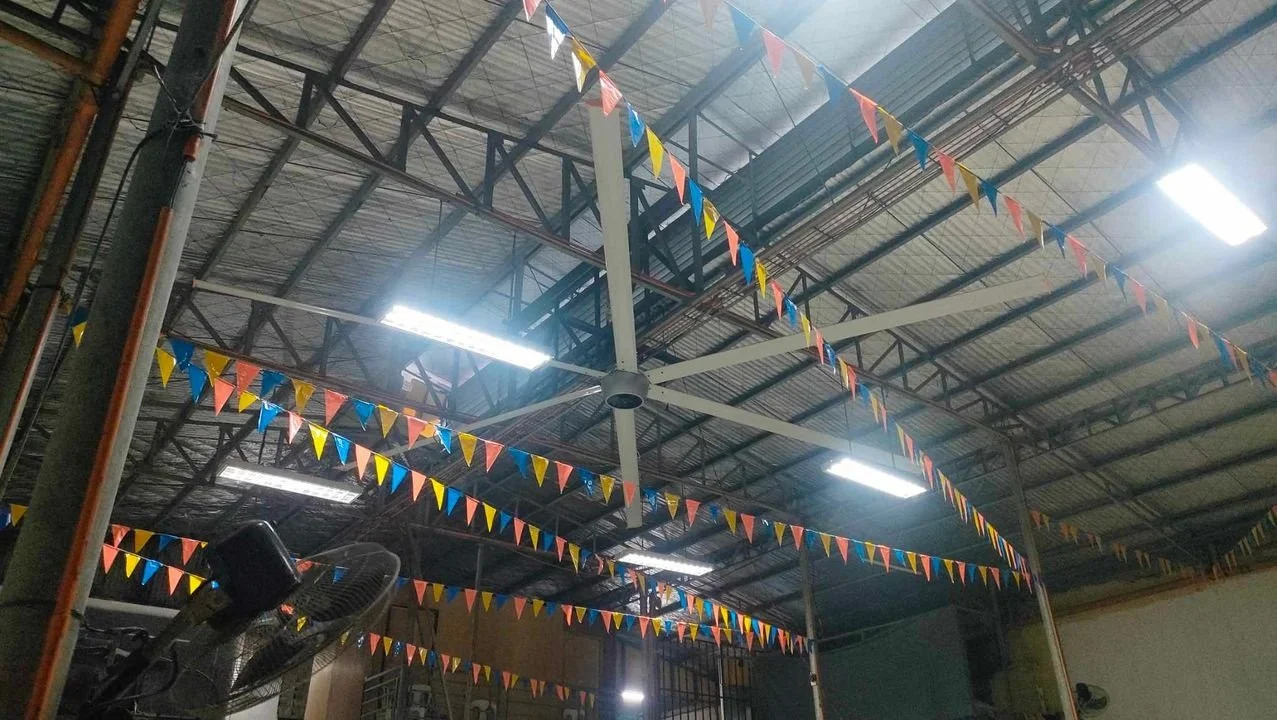 Indoor space with a metal roof, decorated with colorful triangular pennant flags, and ceiling fans with blue blades.