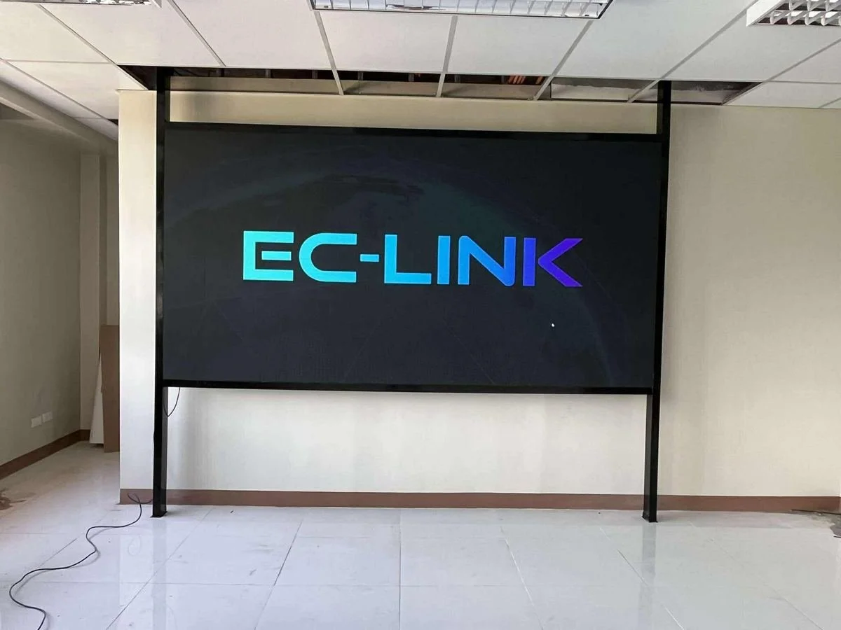Large digital screen displaying the logo 'EC-LINK' in gradient blue and purple colors, situated in a modern office or conference room with white tiled floor and suspended ceiling.