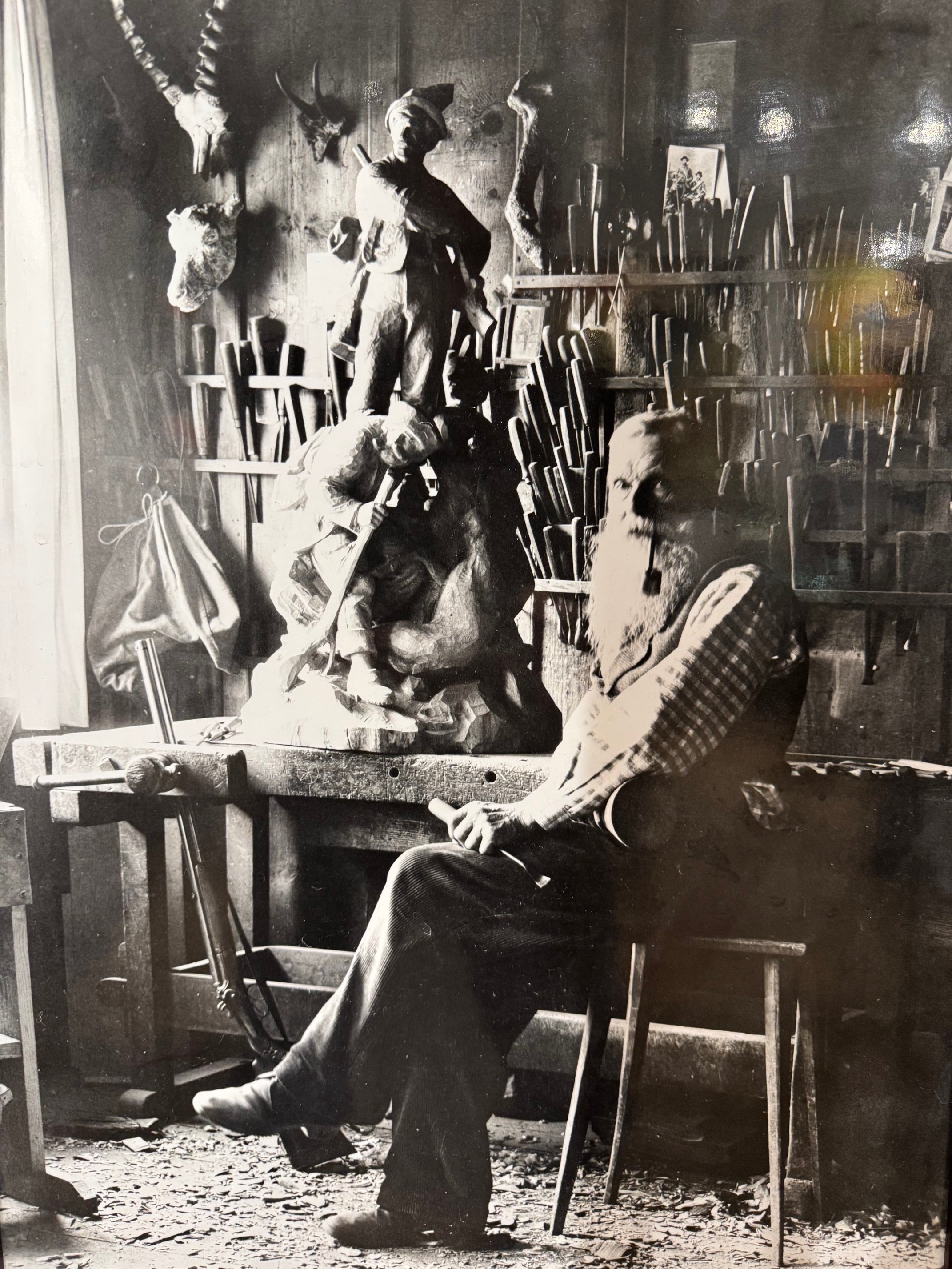 Brienz carver Johann Huggler at his workbench carving a hunting group, with chisels and trophies behind — Daniels Antiques