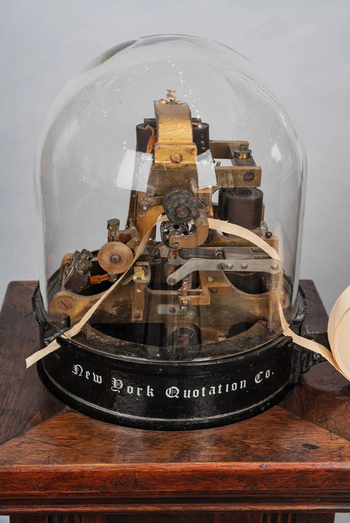 Stock ticker mechanism under glass dome, New York Quotation Co base