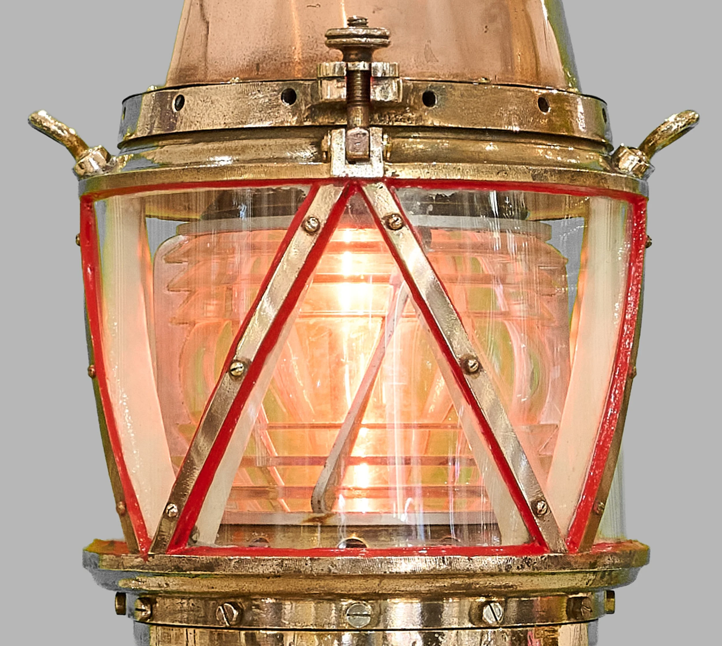 Stepped Fresnel optic glowing within red harbor beacon lantern and brass guards — Daniels Antiques