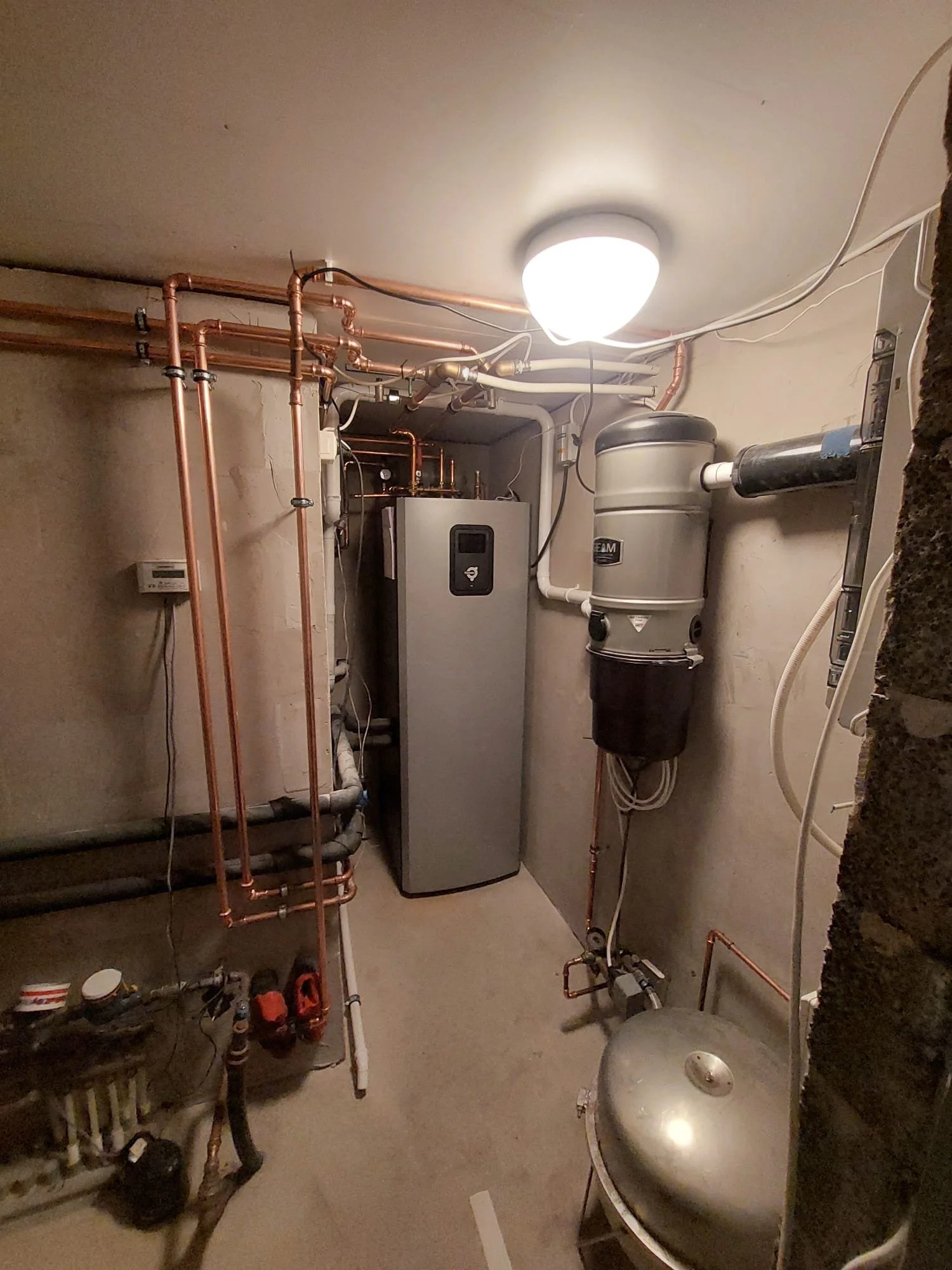 Huone täynnä putkia ja putkistotarvikkeita, näkyvissä vesilämmitysjärjestelmä ja keskusimuri.