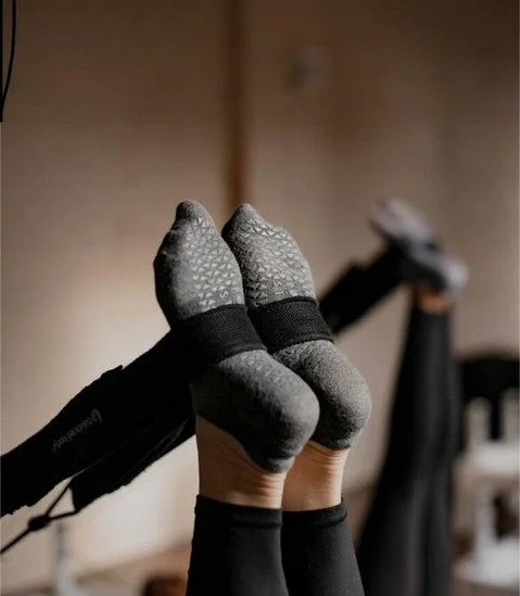 Feet stretching a resistance band while doing reformer Pilates.