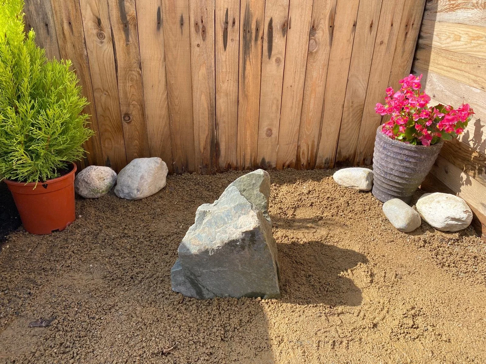 drilled granite rock next to flower pots on light gravel in front of fence panel