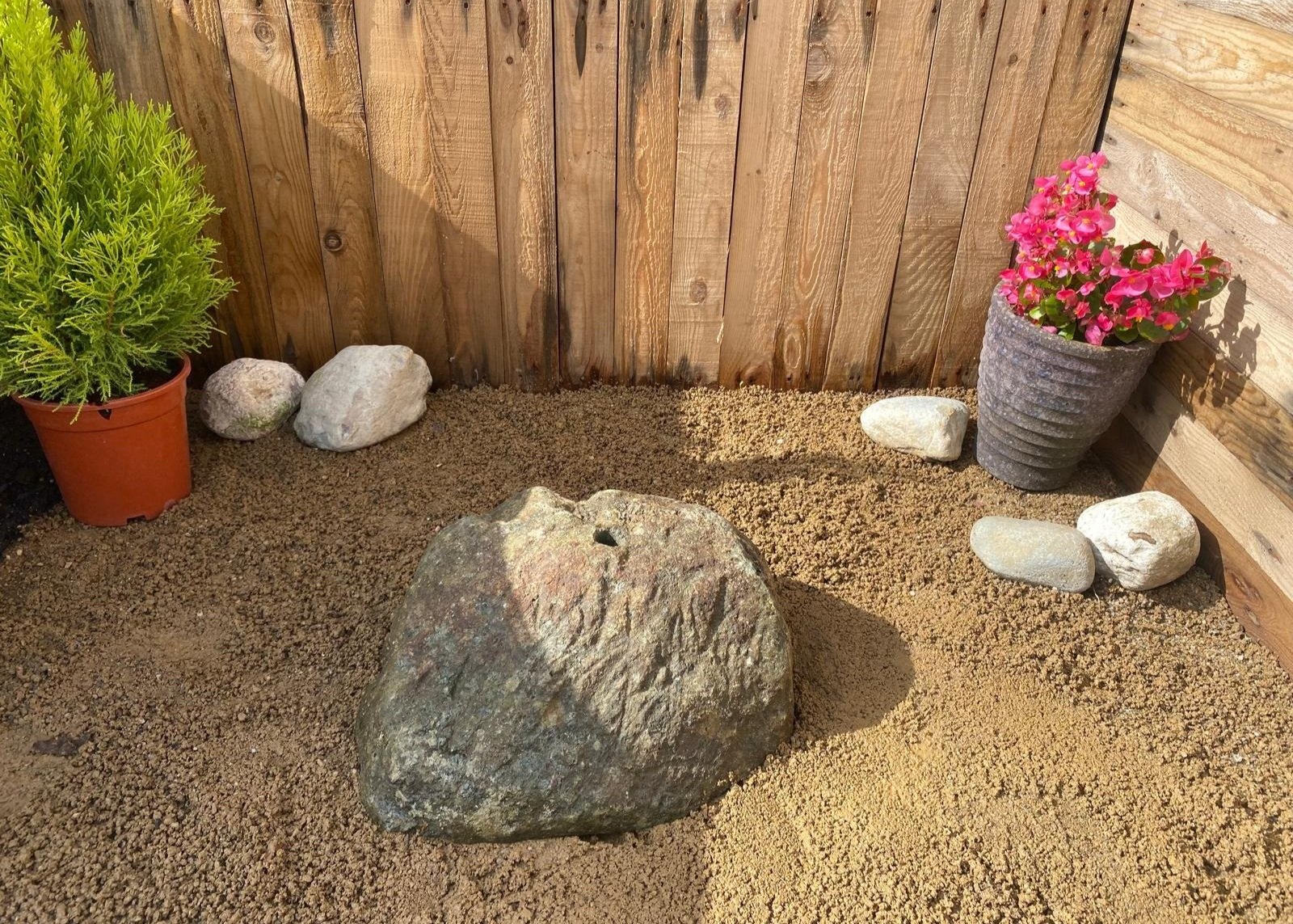 drilled granite boulder on gravel in front of fence panel