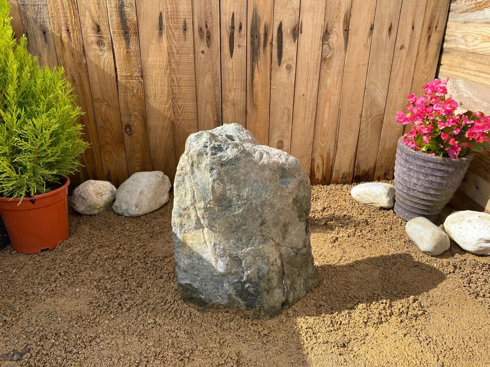 drilled granite boulder in front of fence panel with plant pots either side during the day