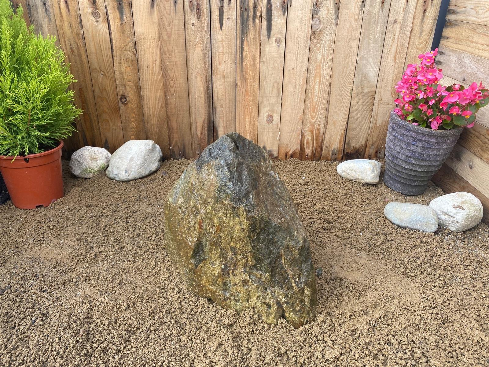 granite drilled boulder in front of fence panel with plant pot either side
