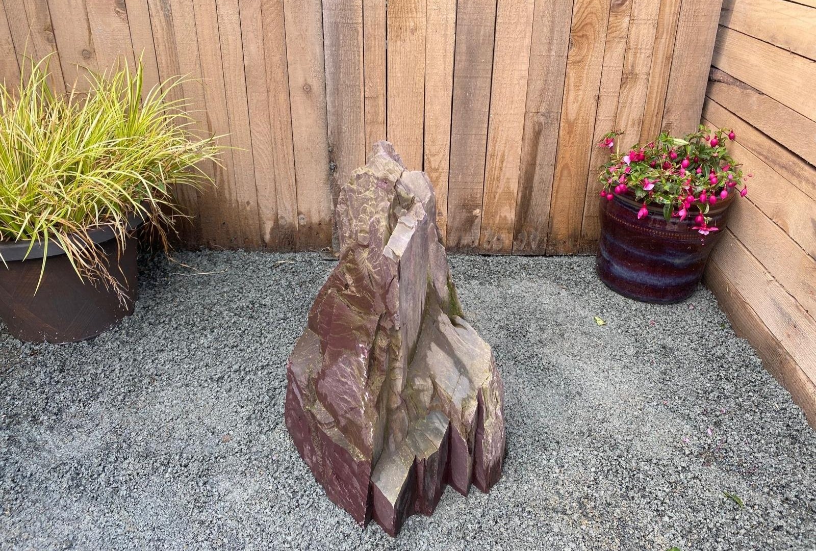 Plum slate monolith in front of fence panelling with plant pots either side of the plum slate monolith