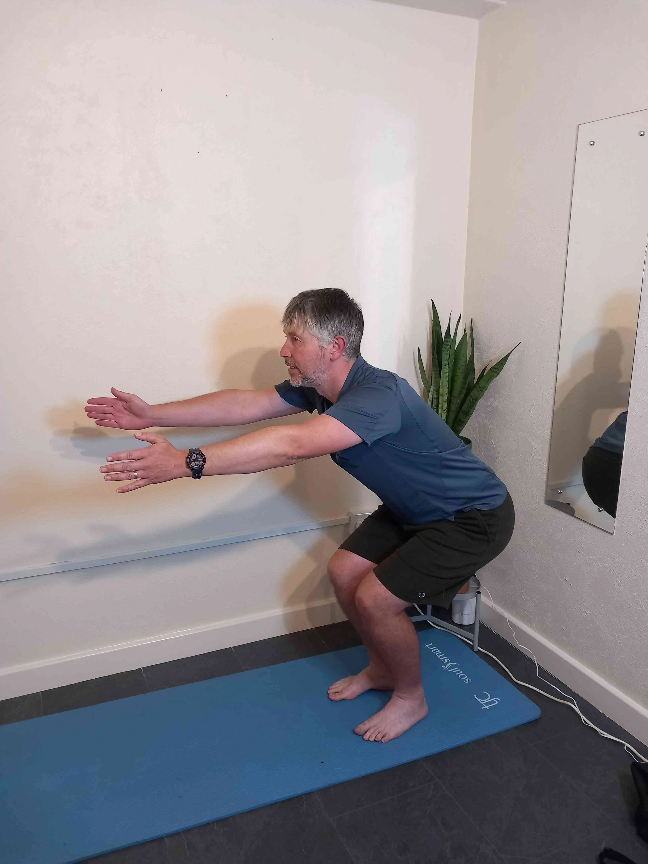 Person performing a squat exercise on a blue yoga mat indoors.