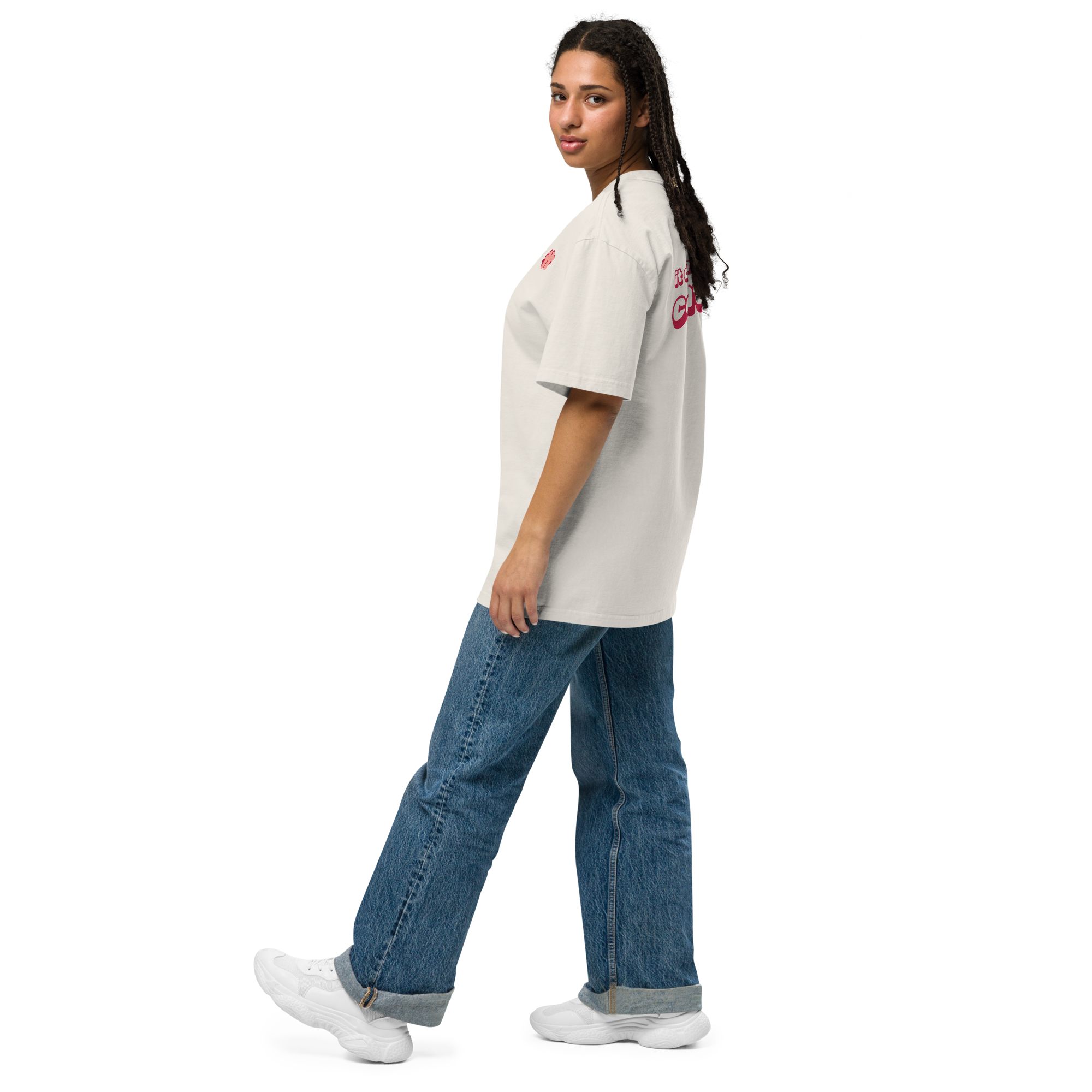 Person standing sideways wearing the cream coloured oversize t-shirt, some of the logo on the front and text on the back is shown.