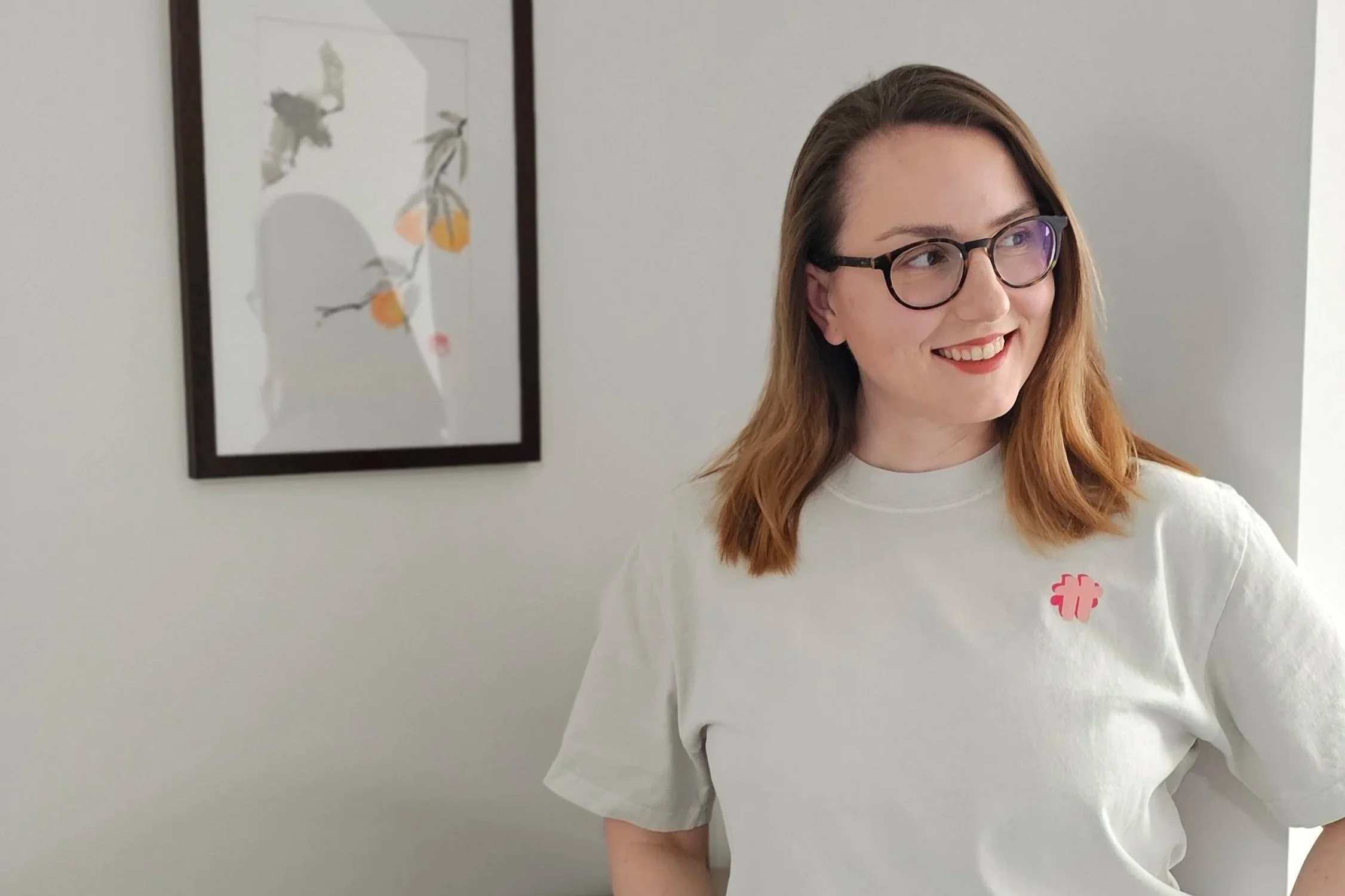 Anikó wearing a t-shirt with the #TeamTranslator logo, standing in front of a painting of a cute bat and looking to the side.