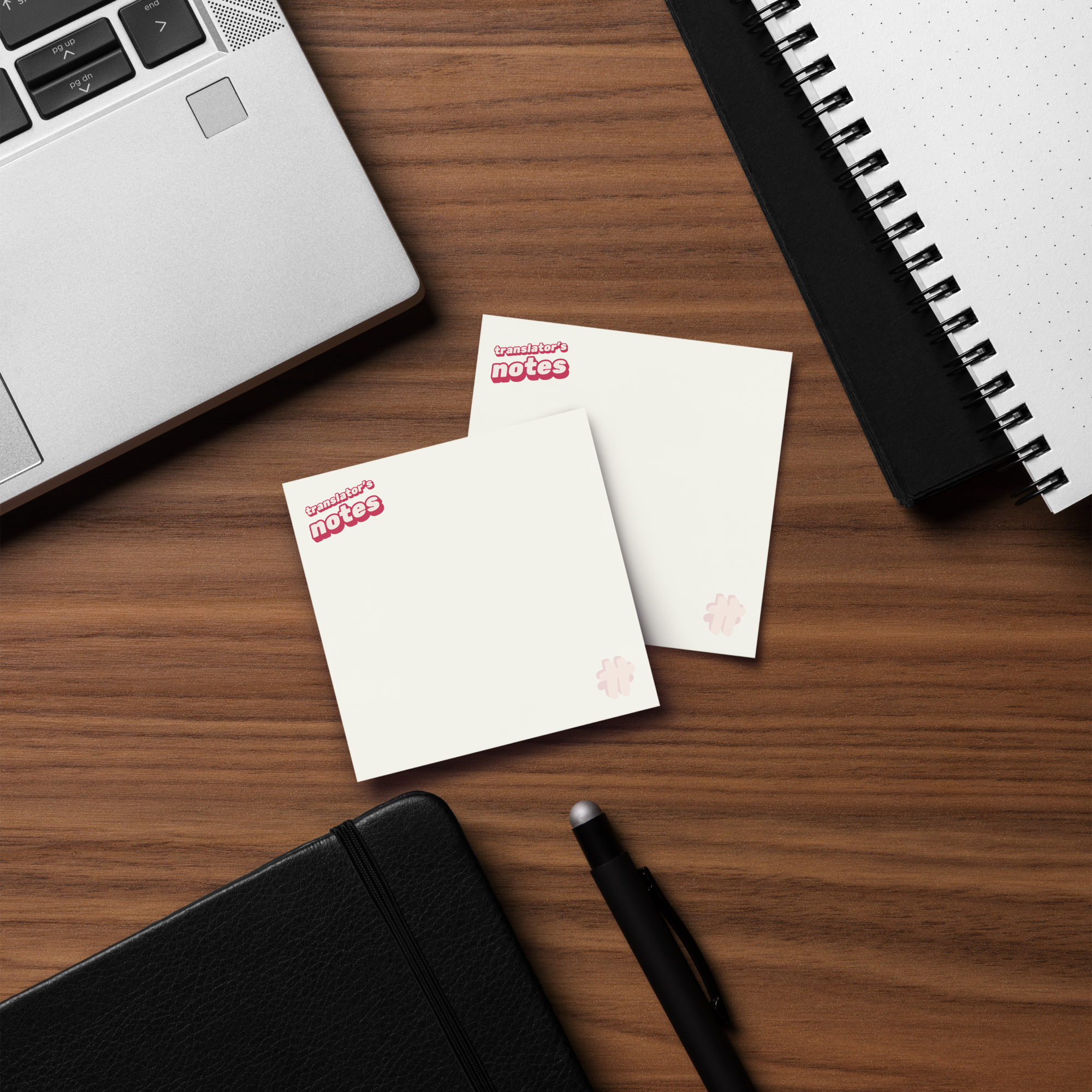 Two packs of #TT translator's notes sticky notes on a desk next to a notebook and laptop.