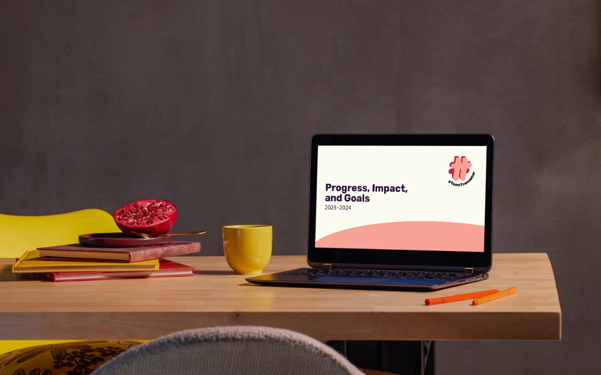 A photo of a laptop on a desk with a preview of the Progress Impact and Growth 2023-2024 document open. The laptop is sitting next to a mug, some books, and half a pomegranate.