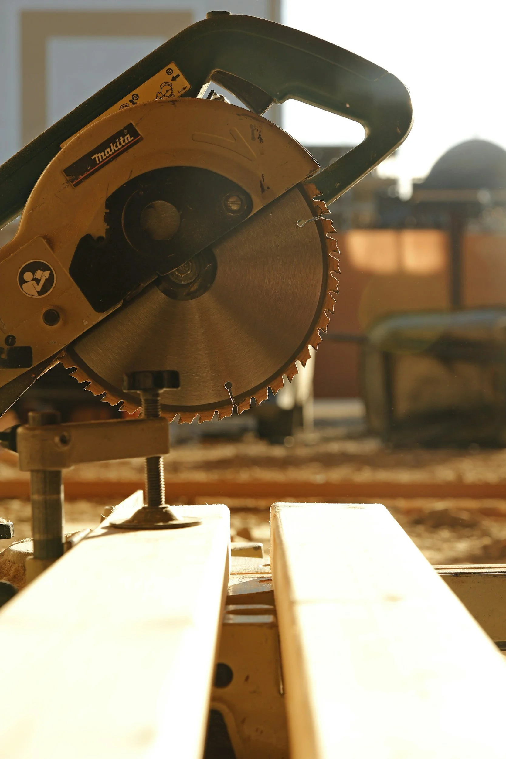 A circular saw blade attached to a power saw in a woodworking shop, with sunlight shining through a window in the background.