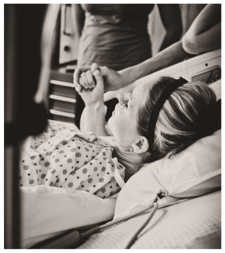 A woman in a hospital bed holding hands with a visitor, in a hospital room.