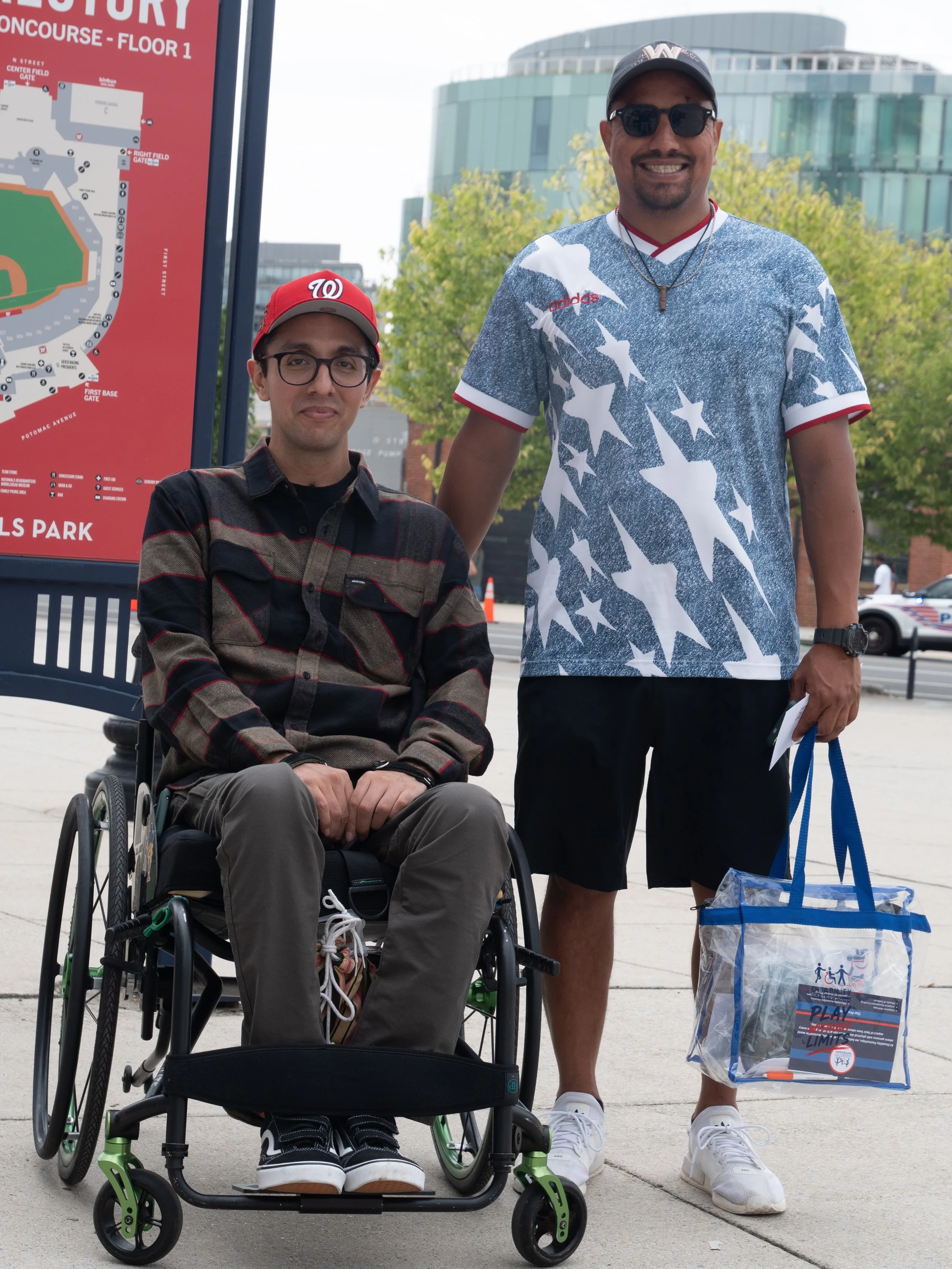 Wheelchair user and companion pose together with Play Without Limits event materials outside Nationals Park