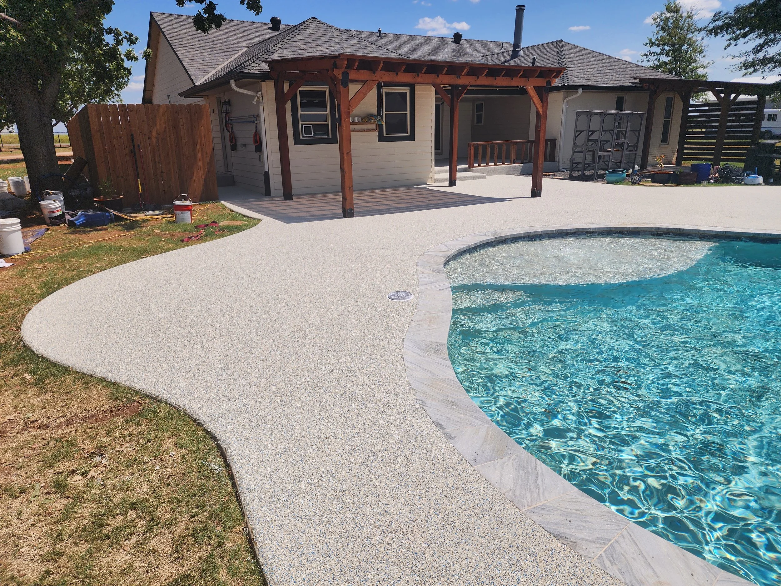 Backyard with a swimming pool, a concrete deck, a house with a patio, a wooden fence, and outdoor storage containers.