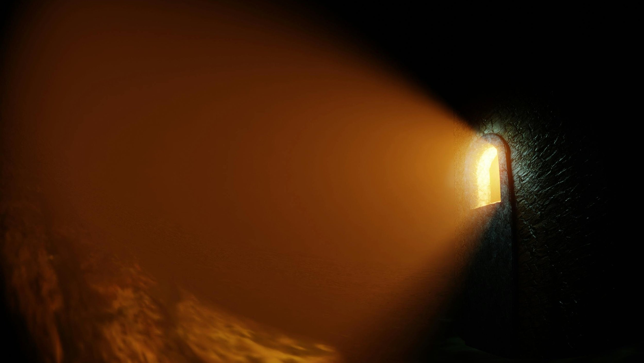 View from inside a dark tunnel looking at an glowing light through a small window opening.