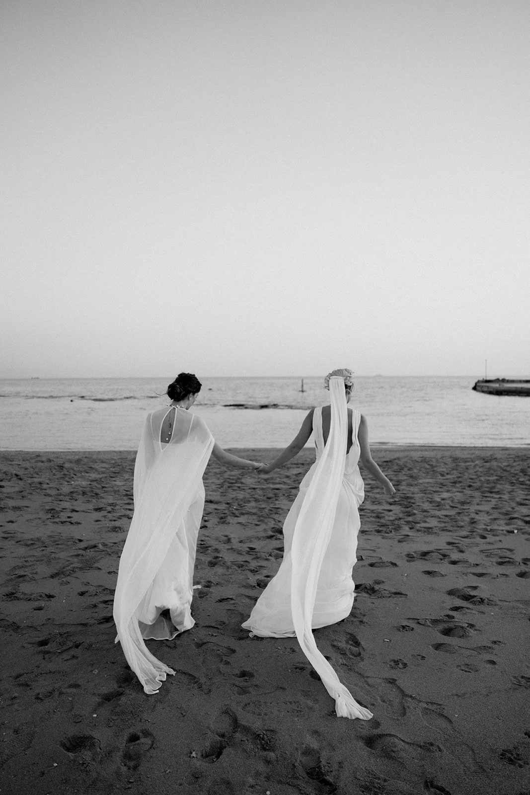 same sex couple photoshoot on the beach running in black and white 