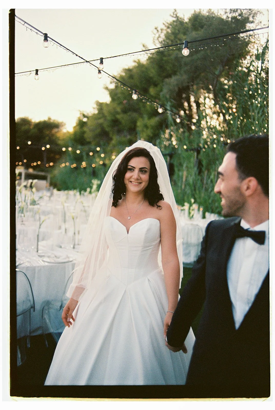 couple smiling with string lights above them 