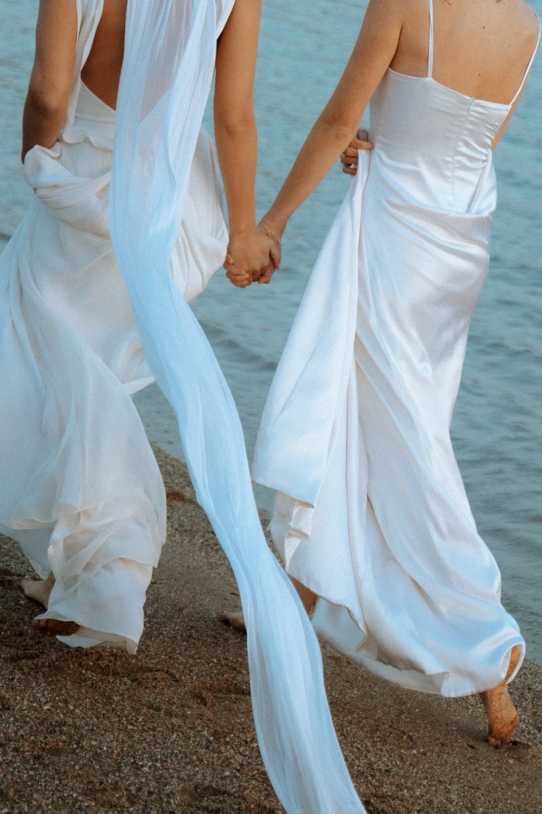 2 brides walking on the beach holding hands 