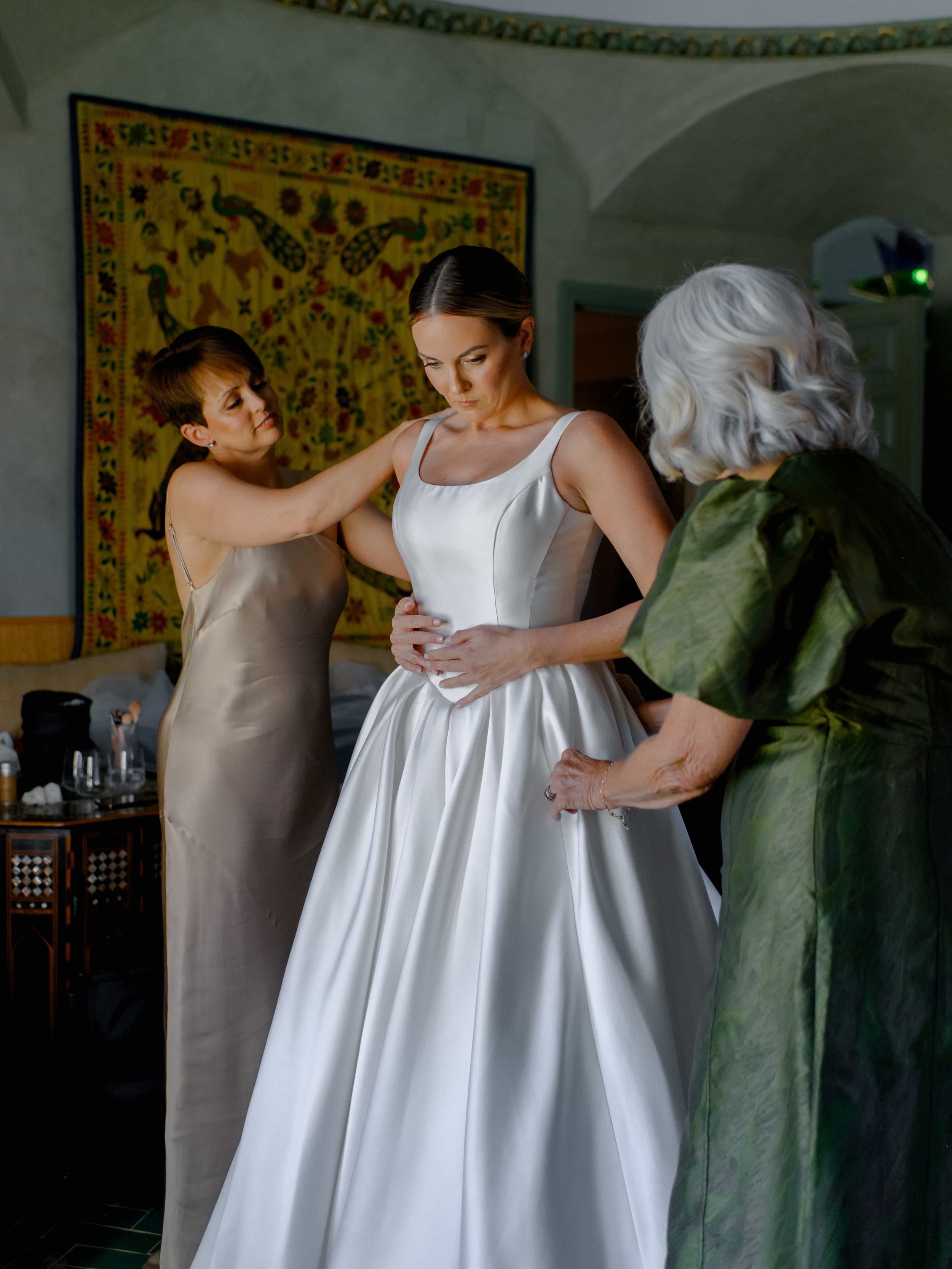 Bridesmaid and mother of the bride helping her get dressed