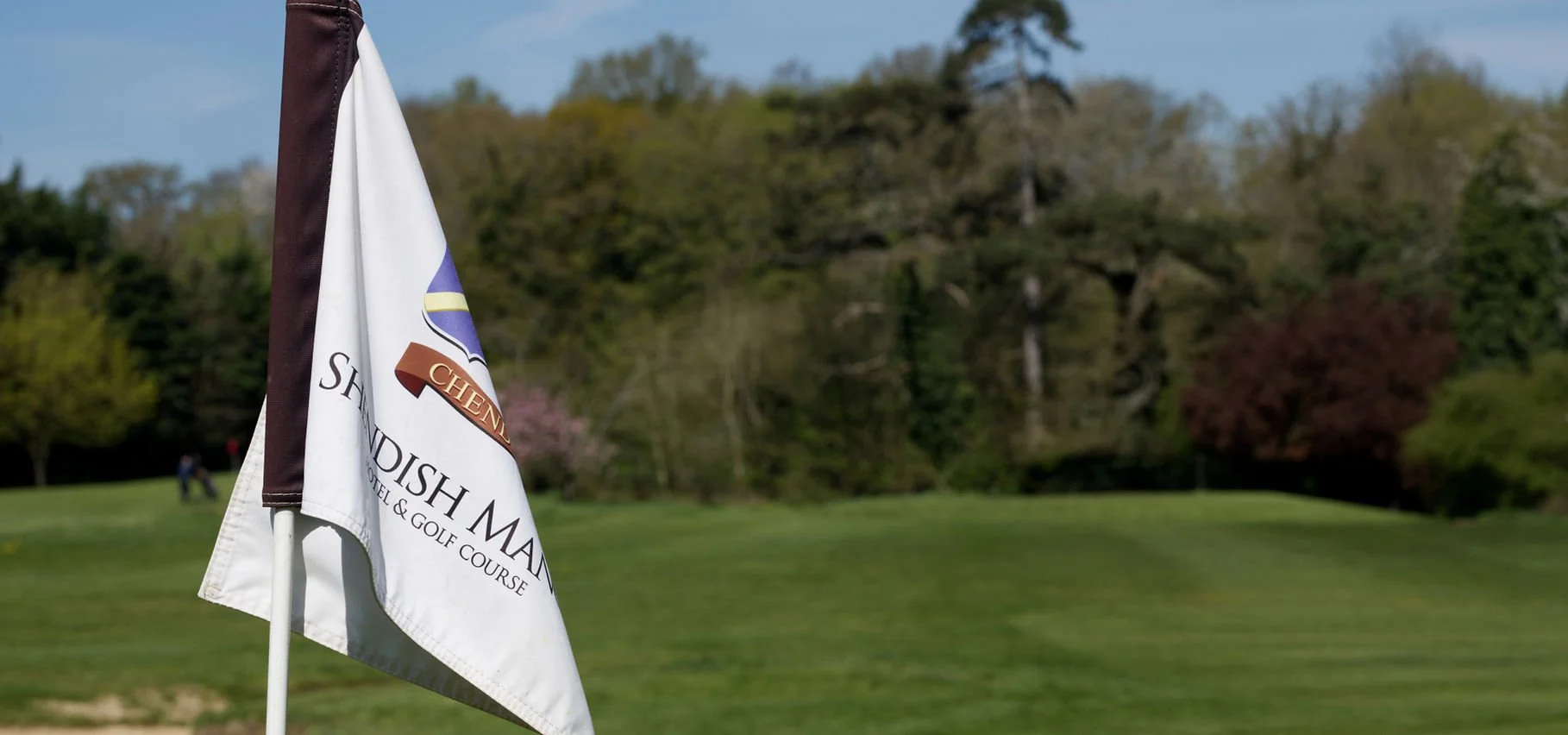 A golf hole flag on a golf course with trees in the background.