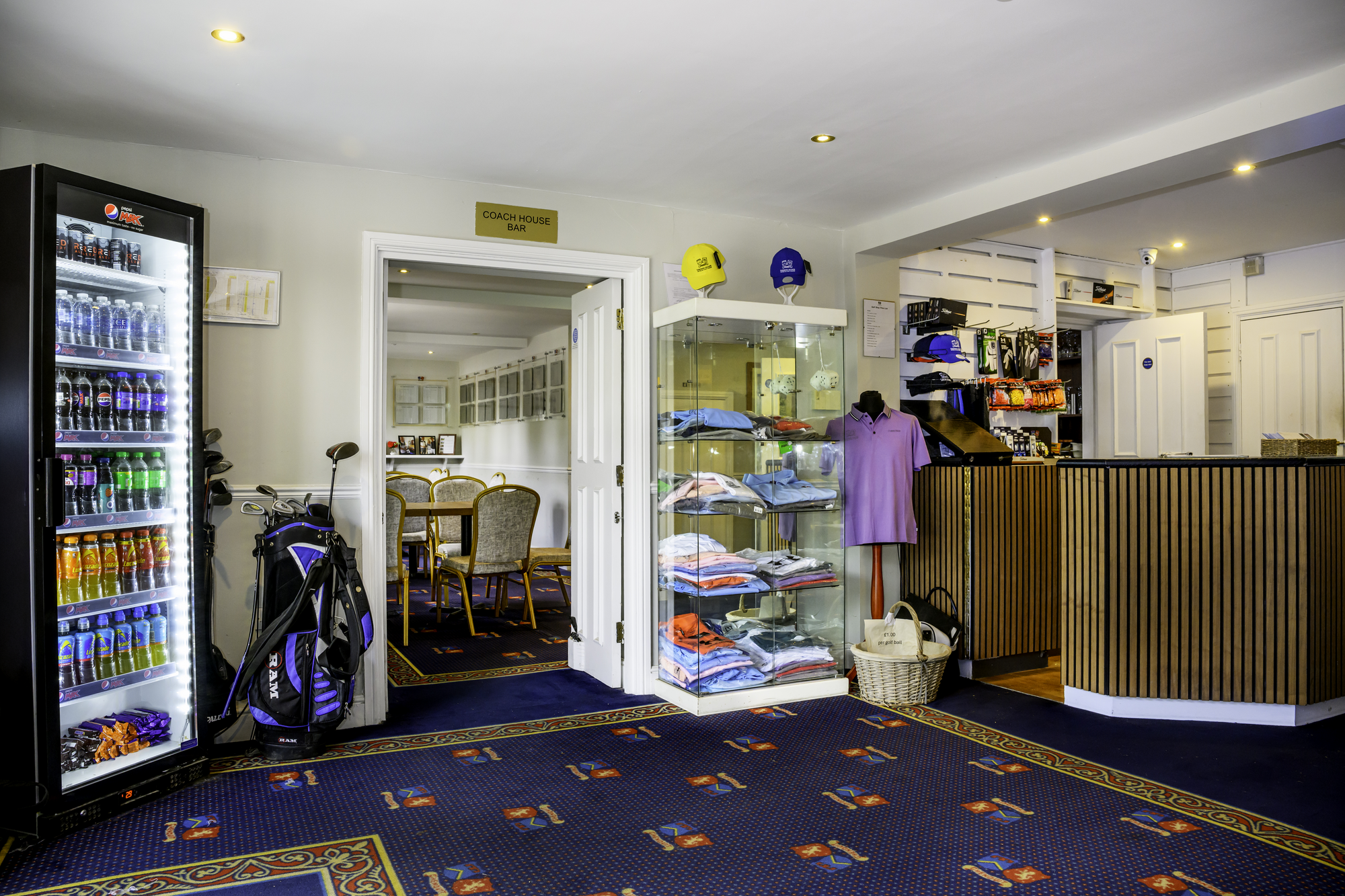 Golf club house interior with vending machine, golf bags, merchandise display, and a reception counter.
