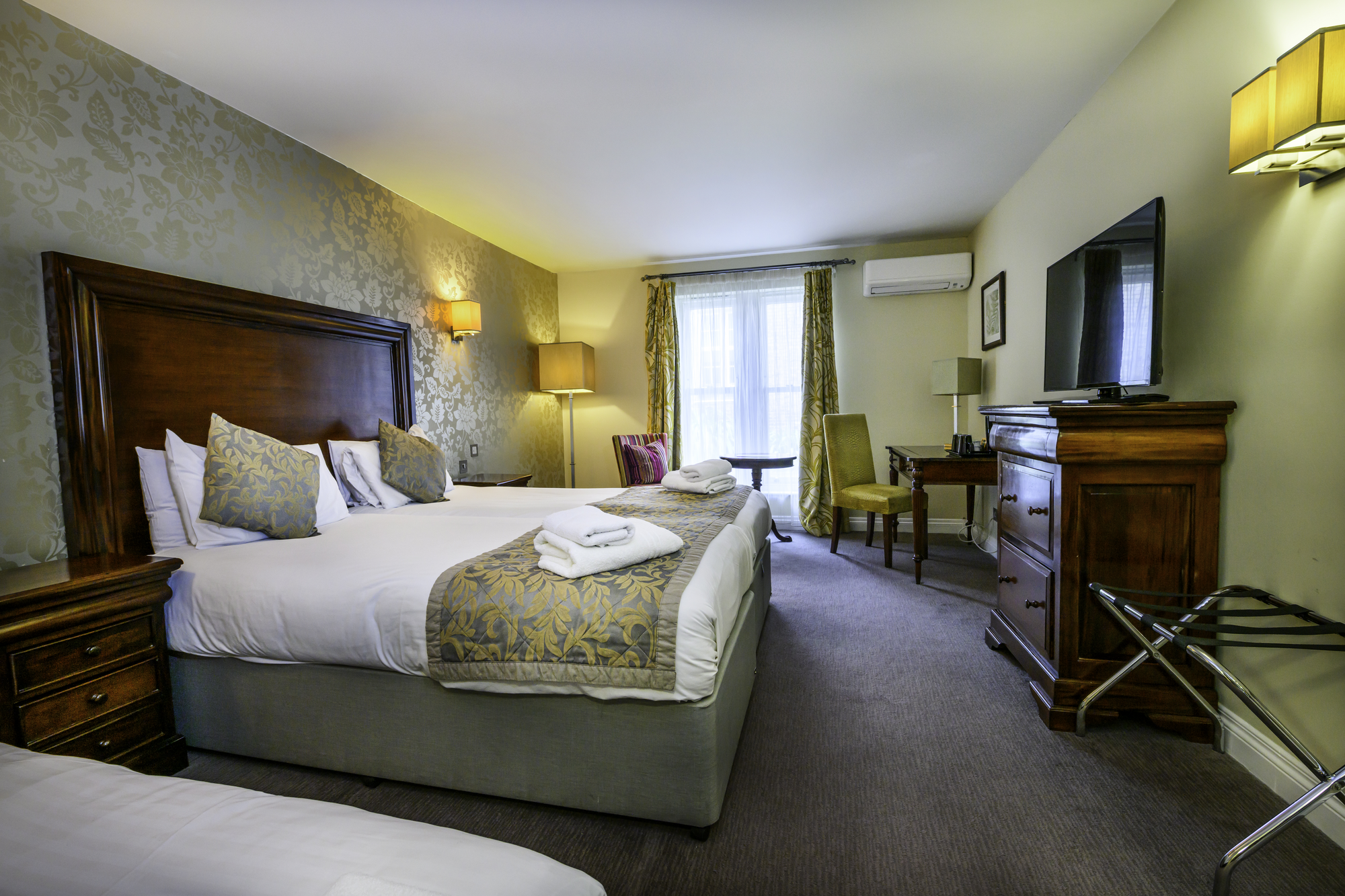 Hotel room with two beds, wooden furniture, television, and a window with curtains.